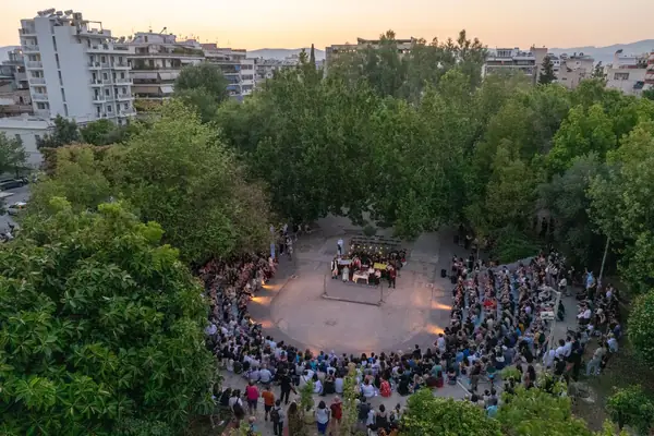 The square from above at sunset: people gather in a circle among the trees