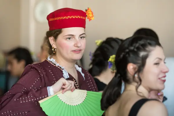 A dancer in a red cap with a green fan, backstage
