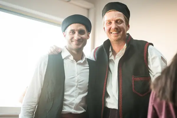 Two dancers in waistcoats and black caps, smiling