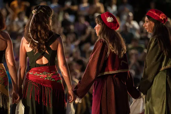 Dancers in costume holding hands, seen from behind