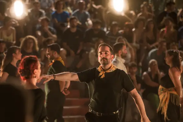 A dancer with a yellow scarf leads the dance through the crowd