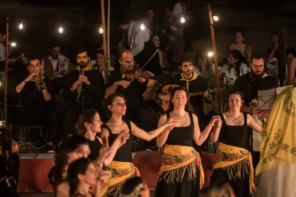 Dancers with yellow scarves dance in front of the musicians