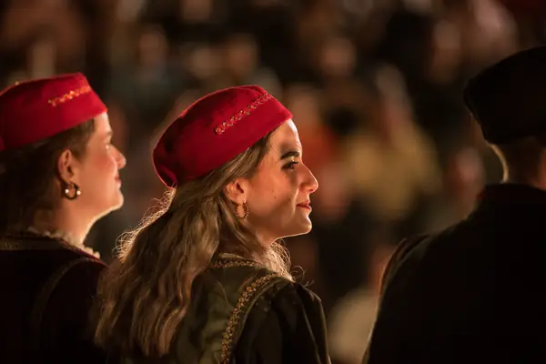 Two dancers in red caps watching the circle