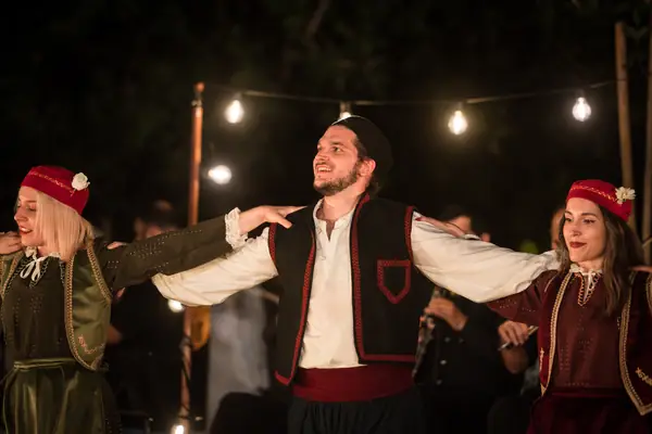 A dancer in a waistcoat dances, smiling, between two dancers