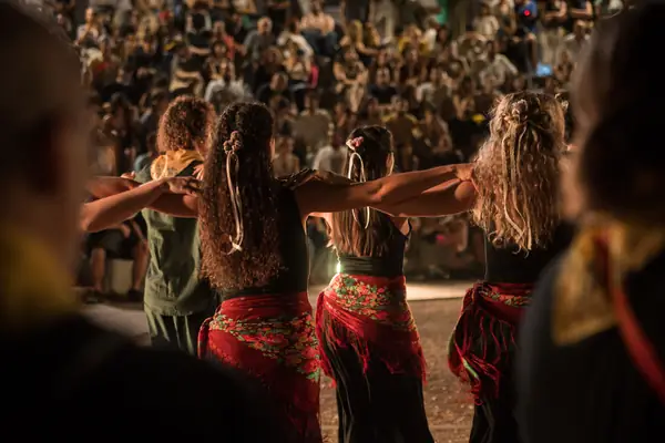 Dancers in red skirts, arms on each other's shoulders, seen from behind